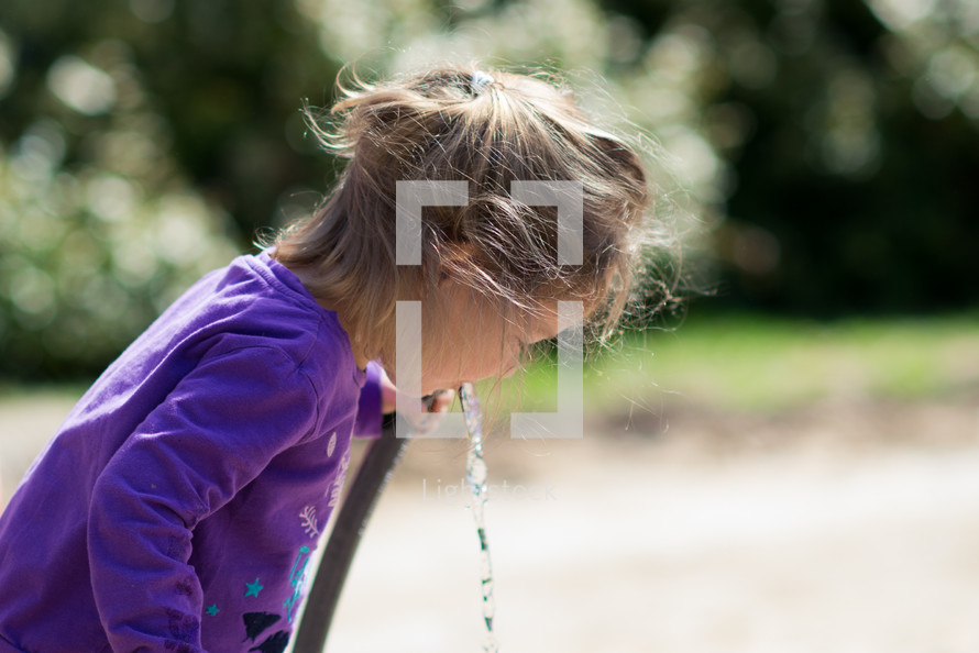 a girl drinking from a water hose 