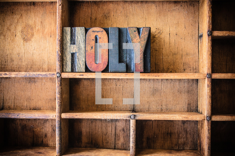 Wooden letters spelling "holy" on a wooden bookshelf.
