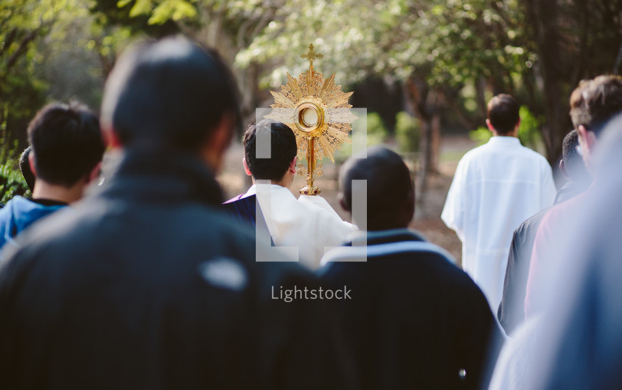 Priest and a crowd walking during a Catholic Eucharistic procession with a monstrance. 