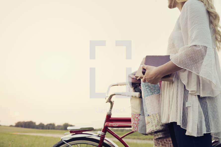 young woman standing next to her bike holding books 