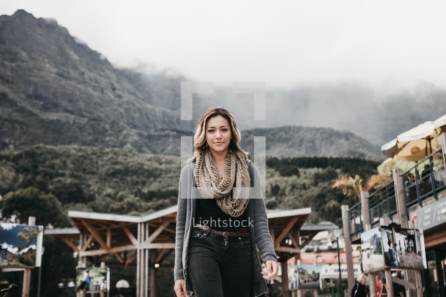 a woman in a scarf and sweater with mountains in the background 