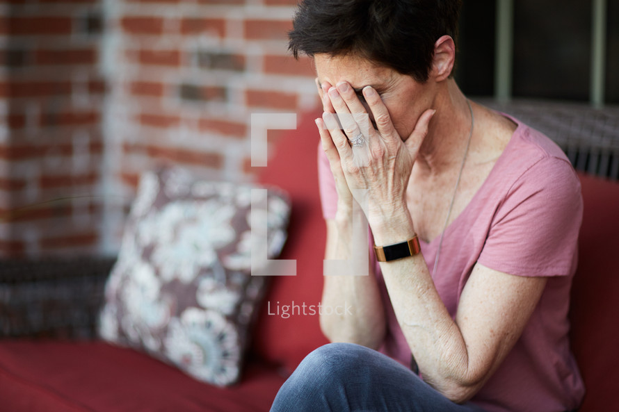 a woman sitting on a porch  covering her face with her hands 