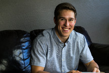 a smiling man  sitting on a couch reading a Bible 