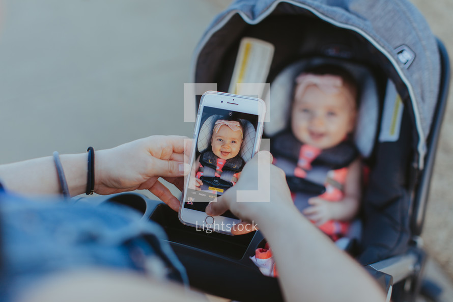 a mother taking a picture of her baby in a stroller with her smartphone 