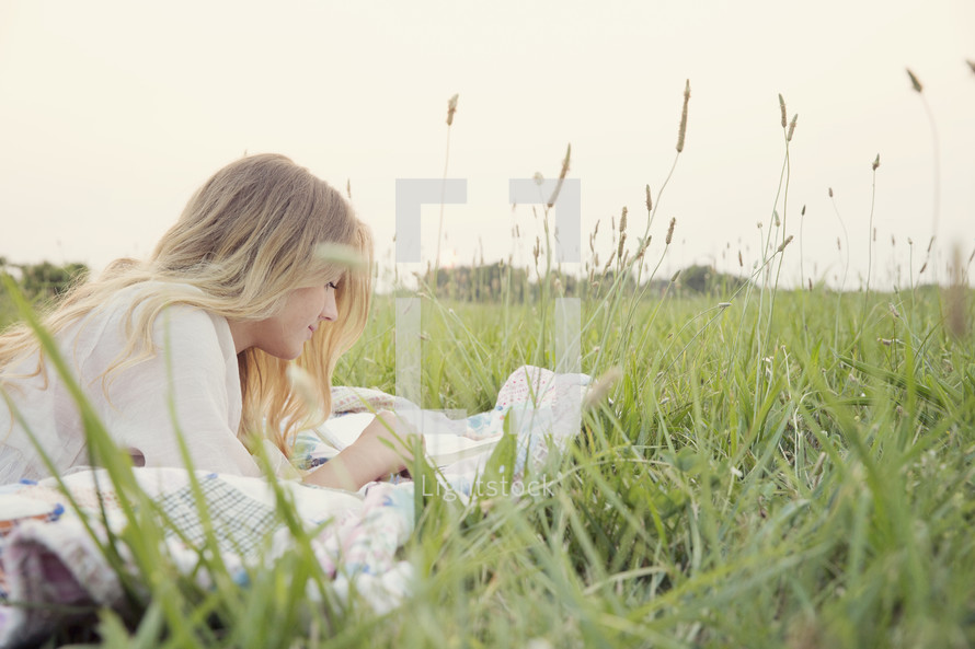 young woman reading on a blanket in the grass 