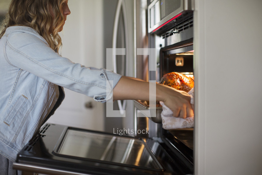 a woman pulling a Thanksgiving turkey out of the oven 