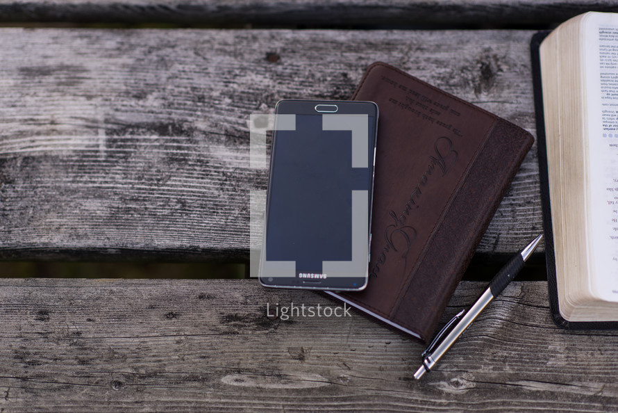 cellphone, journal, pen, and open Bible on a picnic table 