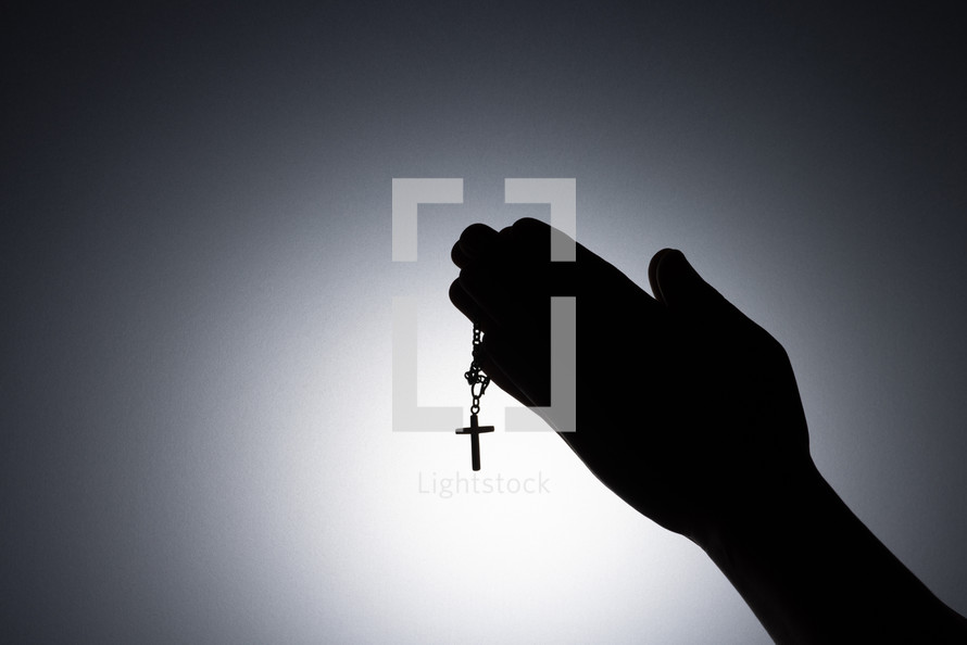Silhouette photo - praying hands holding a rosary