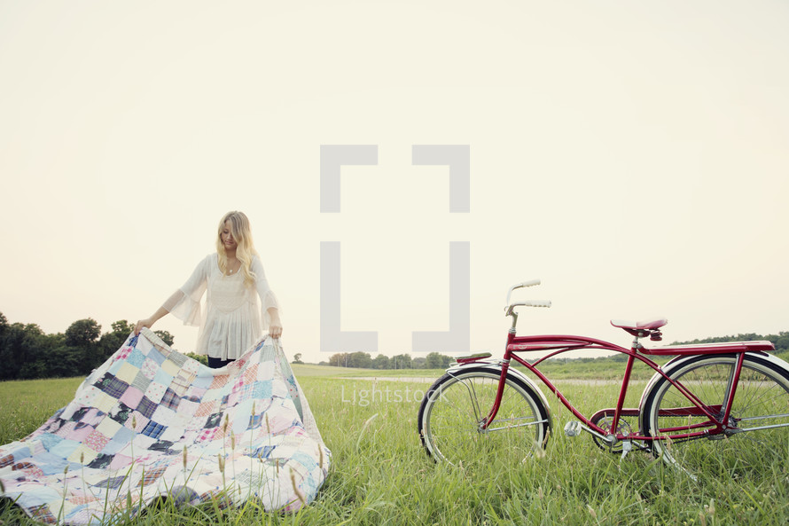 young woman setting up a blanket in the grass standing next to her bicycle 