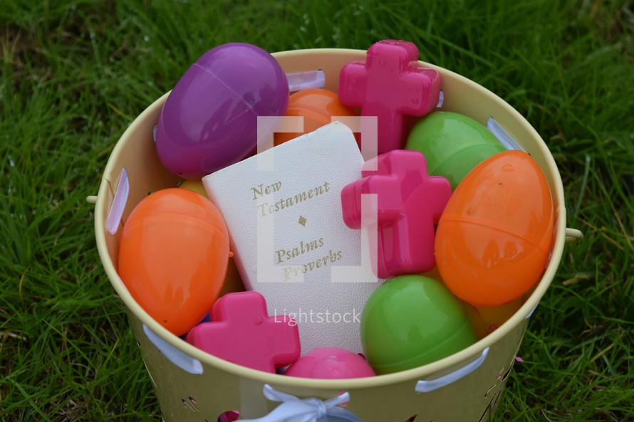 The New Testament Bible in a bucket full of Easter Eggs in lush green grass 