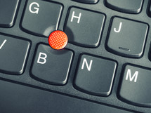 close-up photo of the red pointing stick of on a laptop keyboard