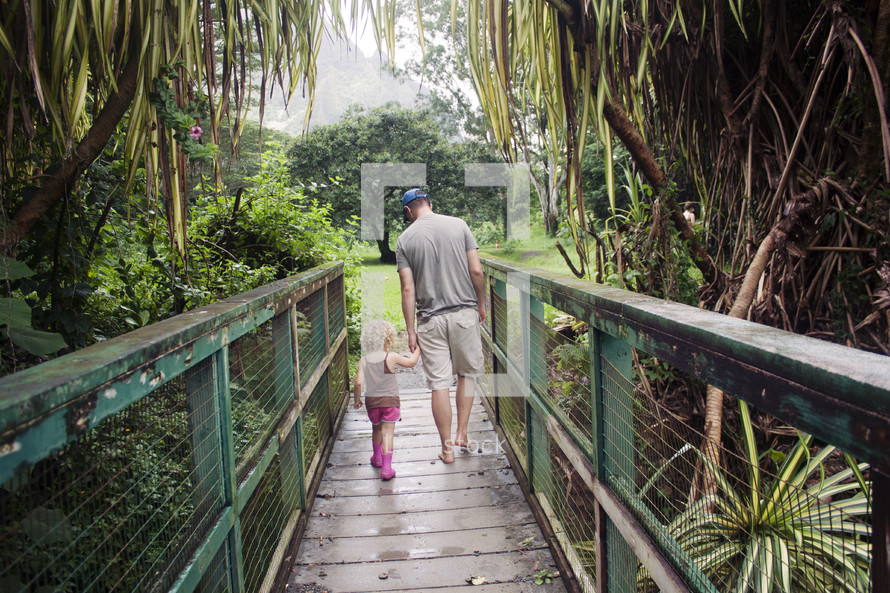 father and daughter holding hands walking across a bridge 