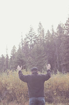 man standing in a field with raised hands 