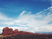 Enormous red rock formations in the desert against a blue sky and clouds.