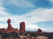 Large red rock formations in the desert against a blue sky and clouds.