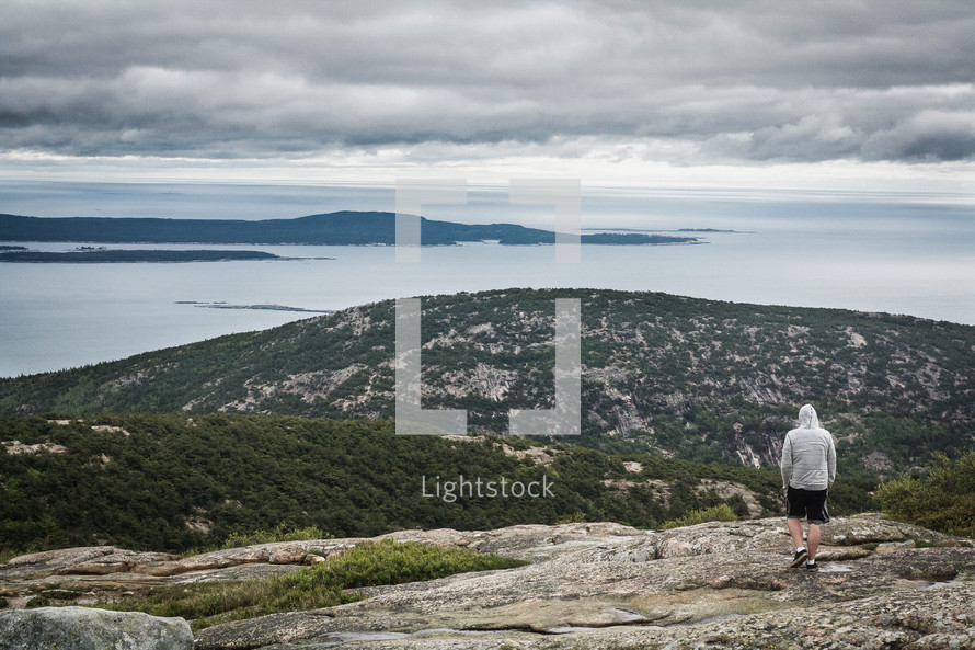 man standing at the top of a mountain along a coastline 