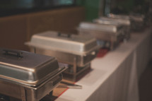 Stainless steel warming pans lined up on a table.