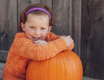 a little girl sitting with a pumpkin 