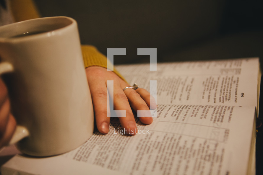 A woman drinking coffee while reading a Bible. 