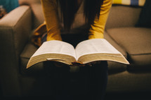 A woman reading a Bible while sitting on her couch. 