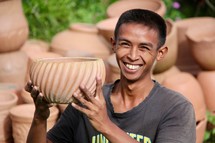 a young man holding up a clay pot 