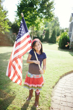 girl child holding an American flag in front of her house