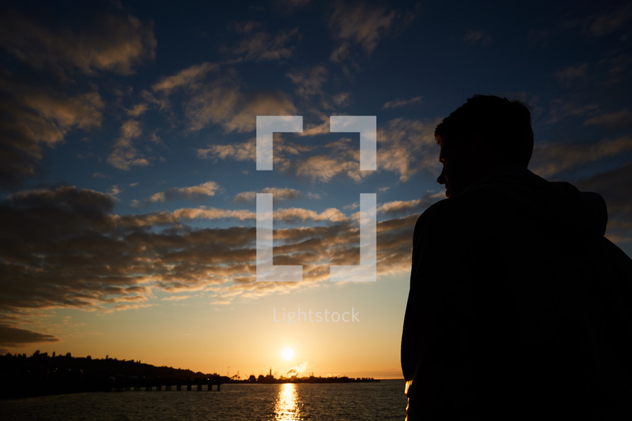 silhouette of a man looking out at the water at sunset 