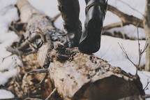 a woman in boots walking on a fallen tree log 