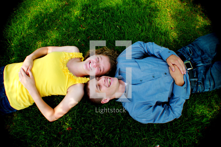 Boy and girl laying opposite of each other in the grass; their heads touching