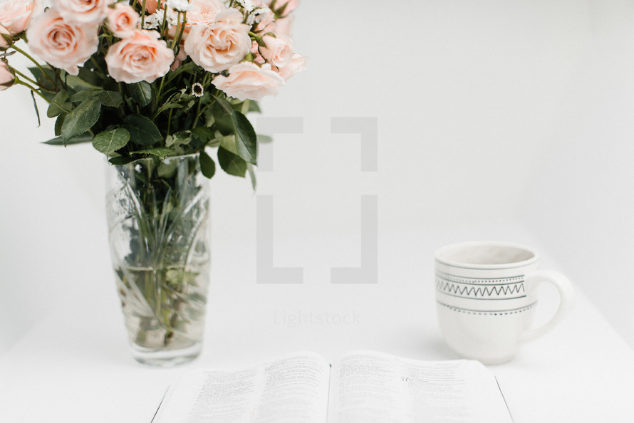 open Bible, coffee cup, and flowers in a vase on a white background 