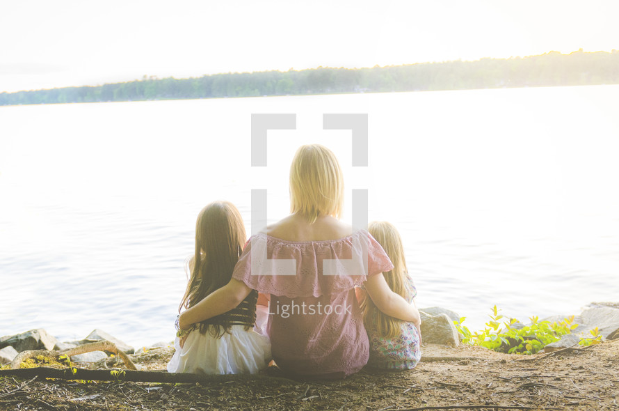 a mother and her daughters sitting at a lake shore 
