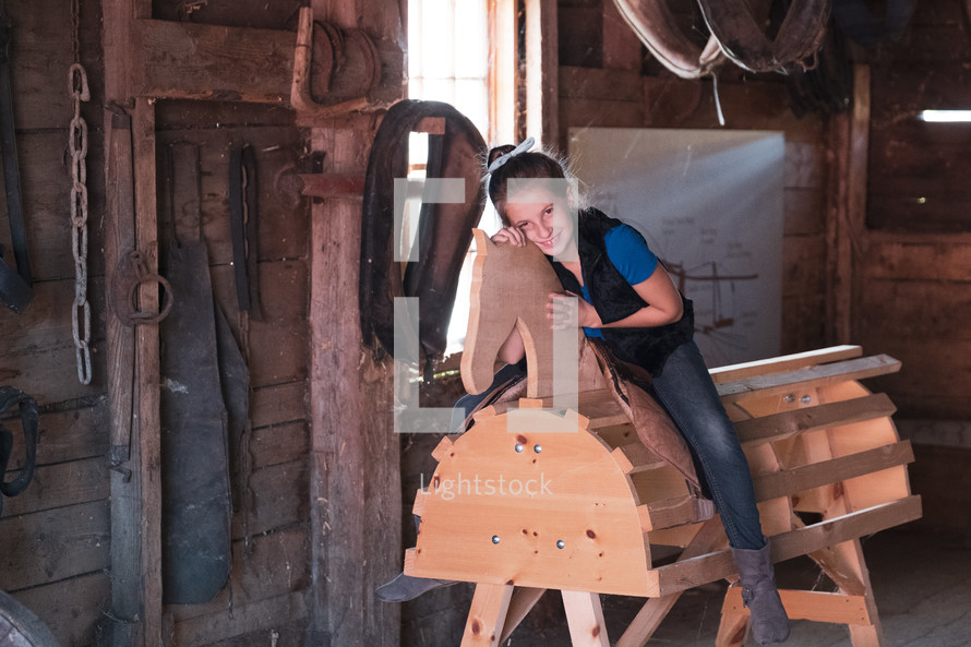 a girl sitting on a wooden horse in a barn 
