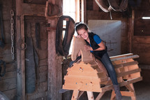 a girl sitting on a wooden horse in a barn 