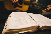 A man playing a guitar while reading a Bible. 