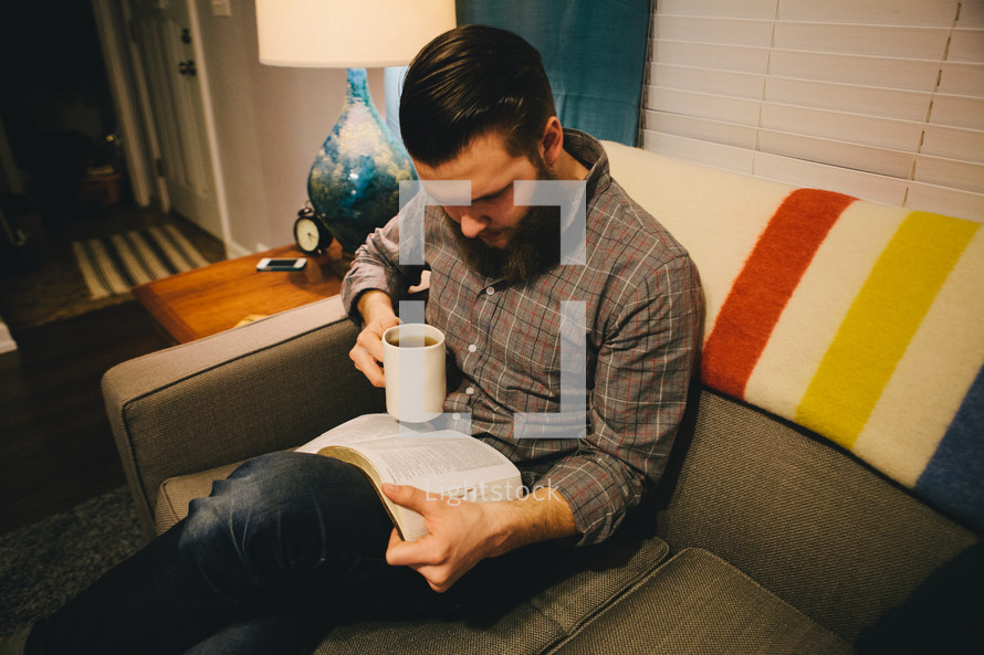 A man reading a Bible while sitting on a couch. 