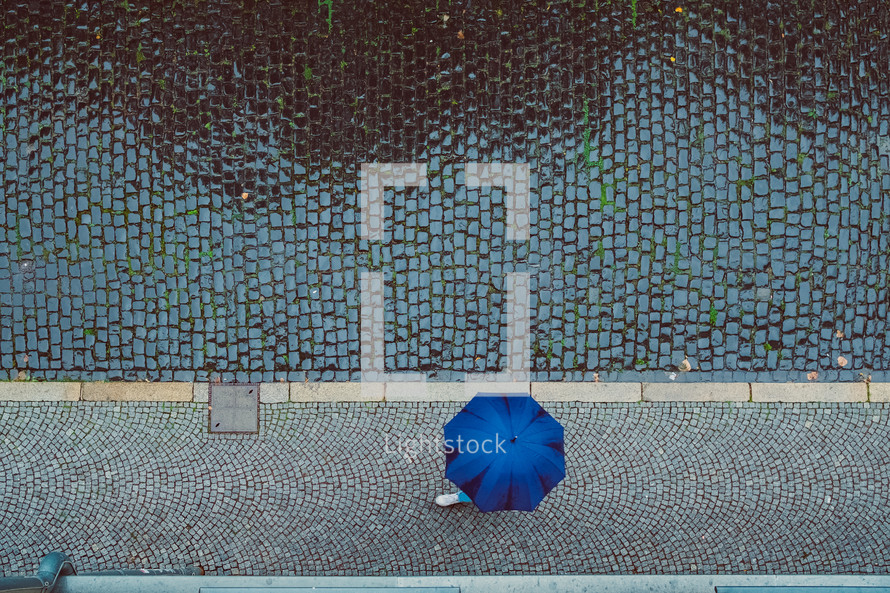 overhead view of a blue umbrella and cobblestone street