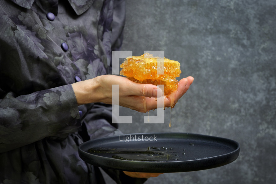 Female Hand Holdong Fresh Honey In Honeycomb over a Plate