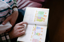 father reading a Children's Bible to a newborn baby 