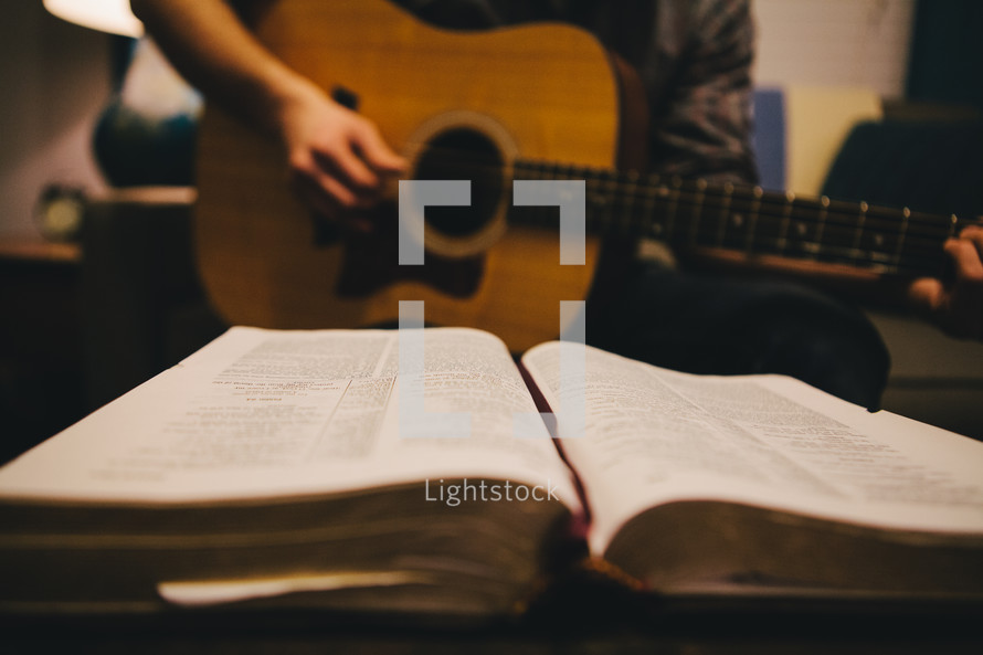 A man playing a guitar and an open Bible. 