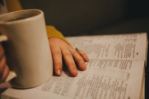 A woman drinking coffee while reading a Bible. 