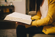 A woman reading a Bible while sitting on her couch. 
