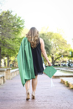 a graduate walking carrying her cap and gown 