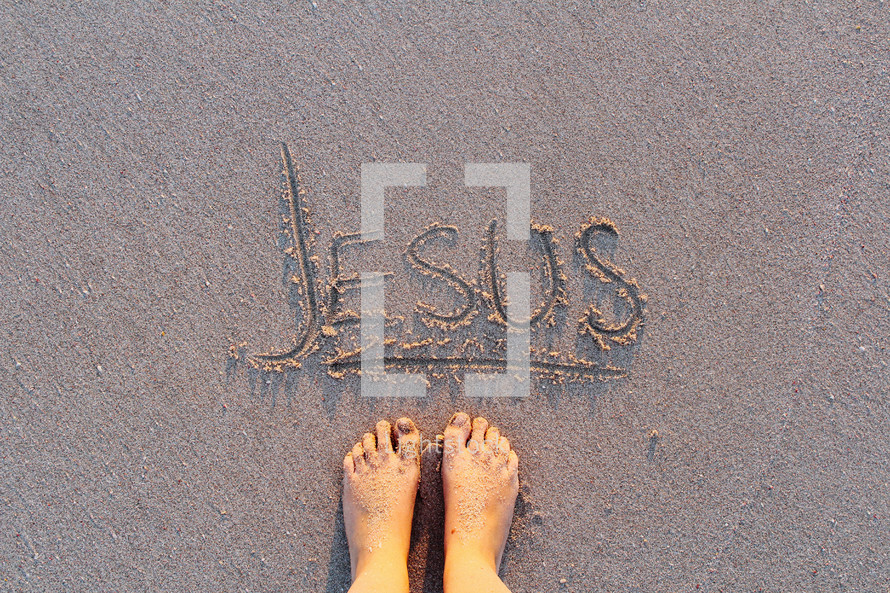 Jesus written in the sands of a beach and bare feet 