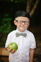 boy child in reading glasses and a hat winking holding an apple 