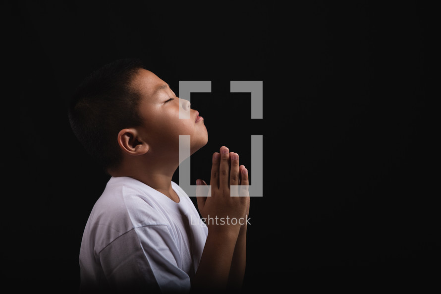 Boy praying to God against a dark background