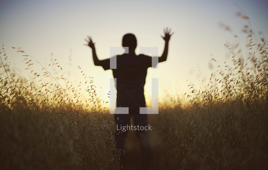 silhouette of a young man with raised hands at sunset 