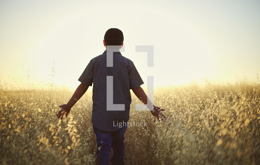 a young man walking through a field of tall grasses at sunset 