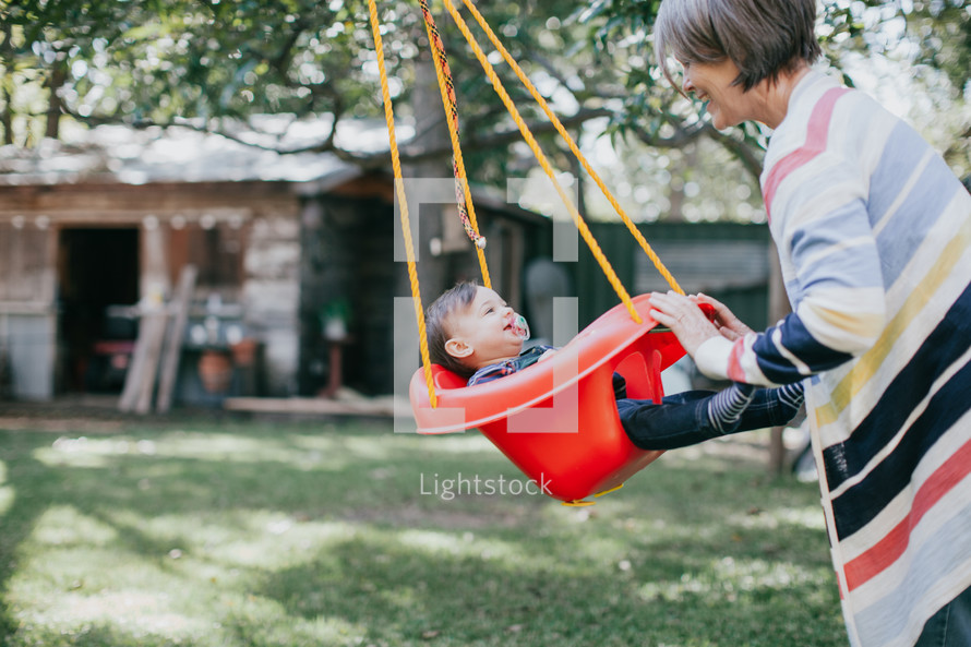 a grandmother pushing a toddler girl on a swing 