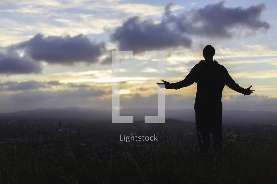 a silhouette of a man standing on a mountaintop at sunrise with outstretched arms 