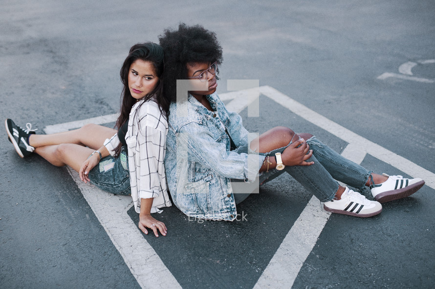 two young women sitting in a parking lot 